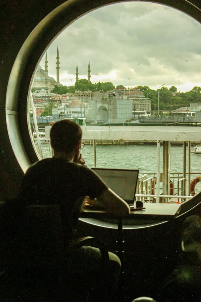 Silhouette of a man working on a laptop with a view of Istanbul cityscape through a circular window.